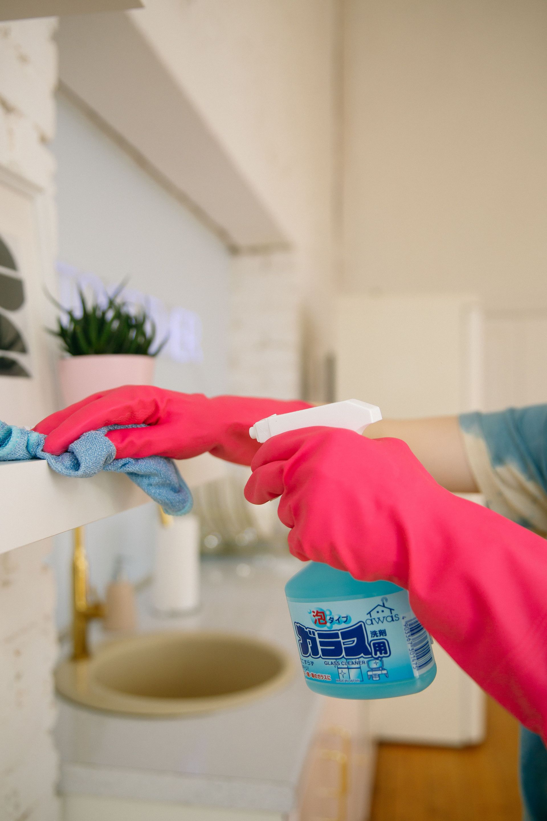 Person using spray bottle and cloth for cleaning a kitchen shelf, ensuring hygiene and cleanliness.